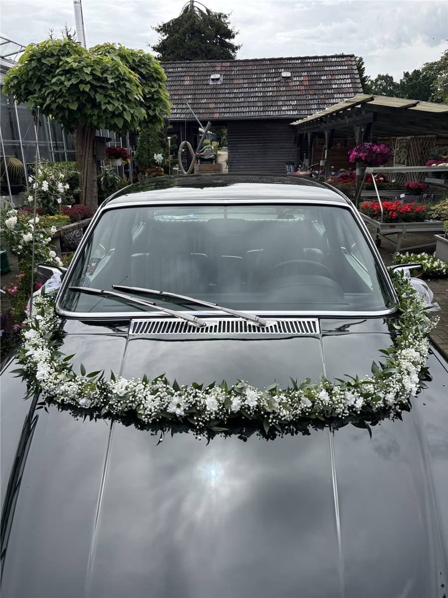 Hochzeitsauto mit Blumengirlande auf der Motorhaube